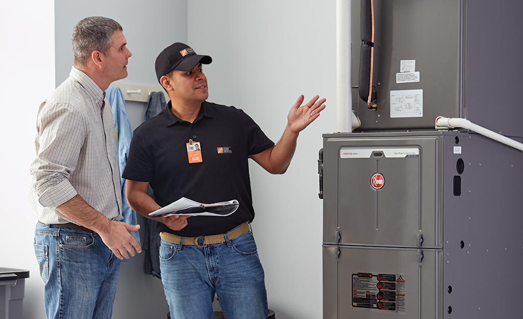 A Home Depot associate standing next a homeowner and gesturing to a furnace.