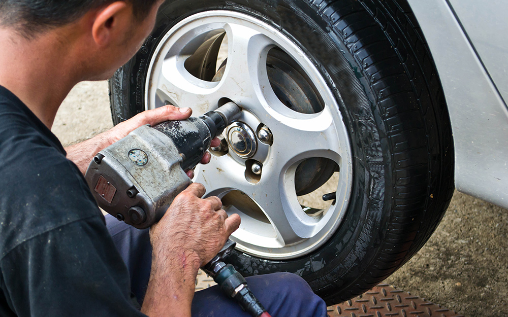 A person tightening lug nuts with a pneumatic wrench. A person tightening lug nuts with a pneumatic wrench.