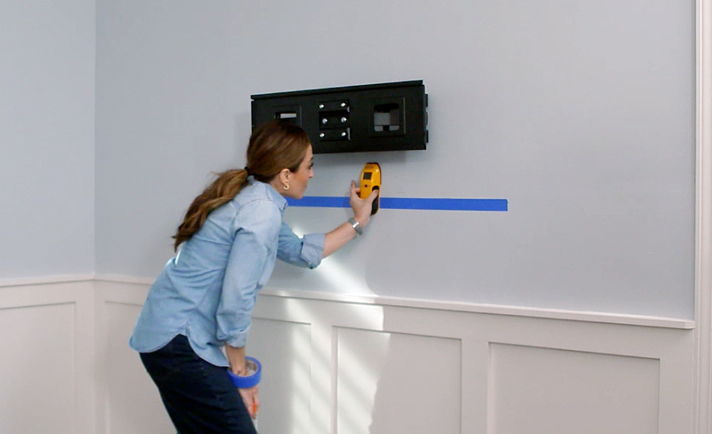 A person reads a stud finder to find studs behind a drywall.