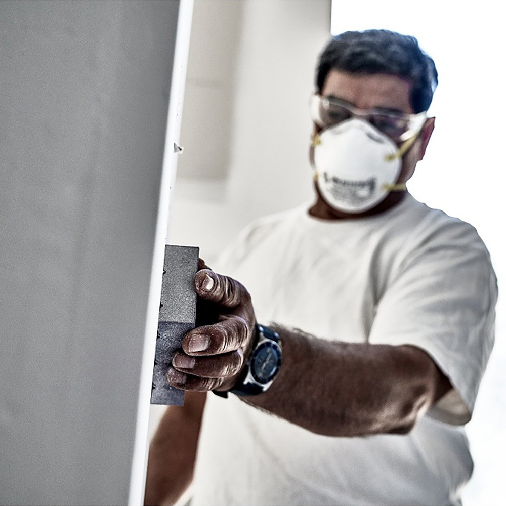 A person sanding drywall with a sponge.