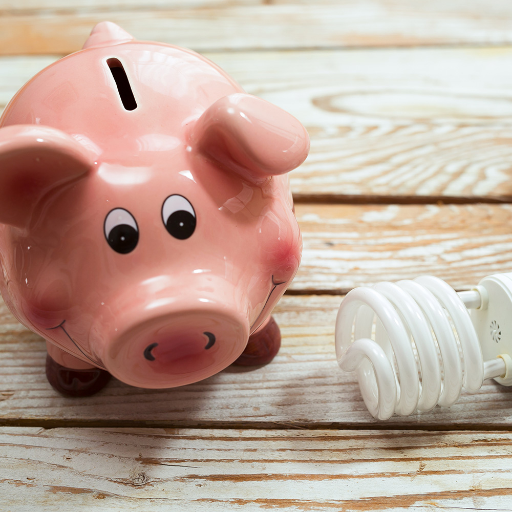 A piggy bank sits on a table near an LED bulb.