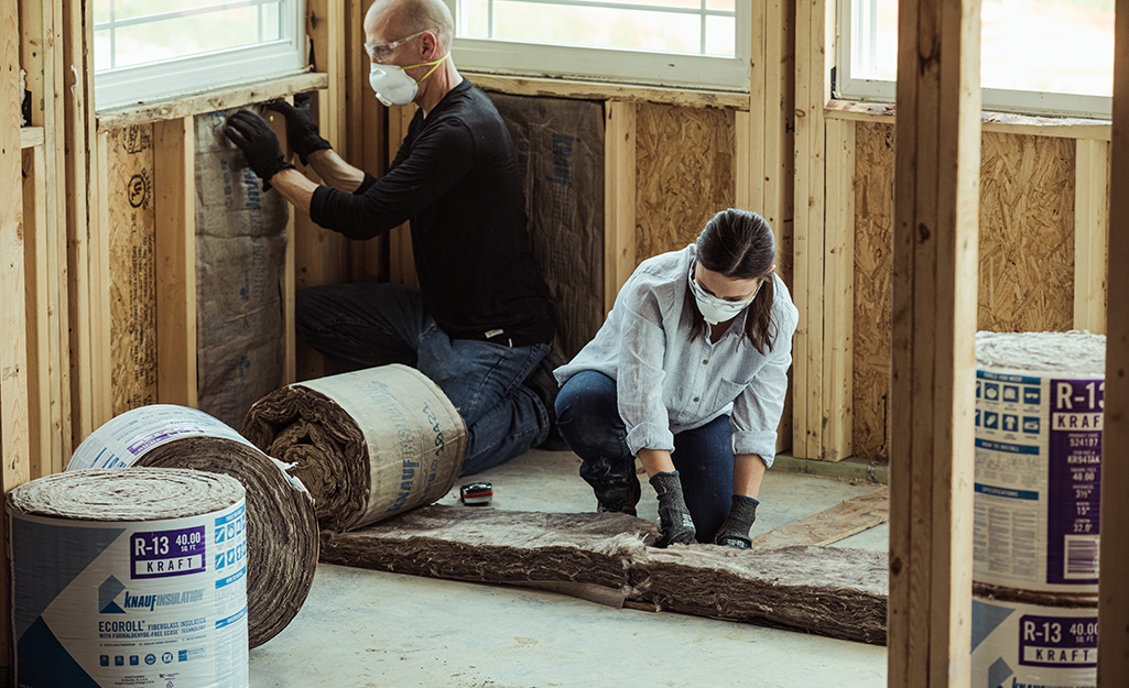 A man and woman install insulation in walls.