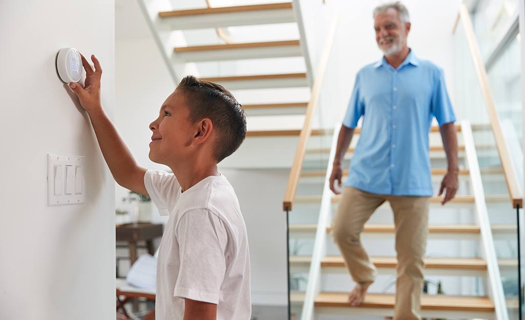 A father watches his young son use a thermostat.