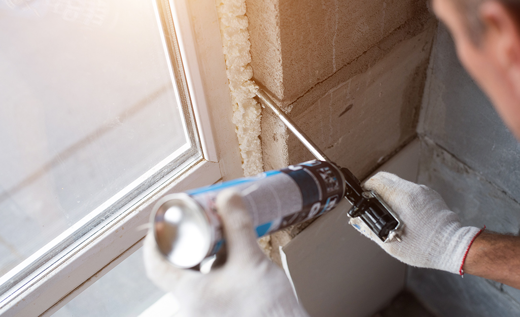 A man uses caulk to insulate windows. A man uses caulk to insulate windows.
