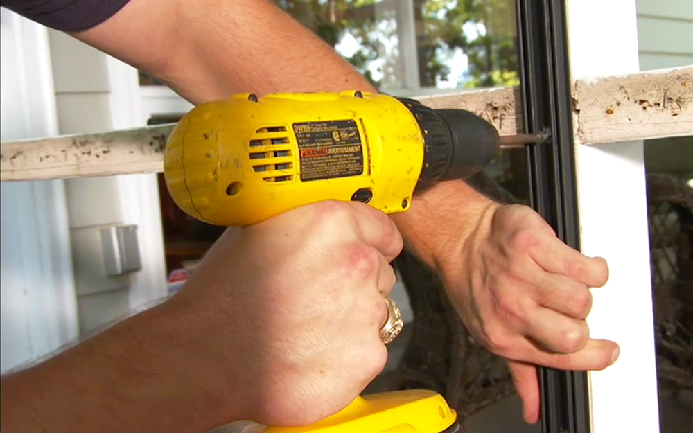 A person using a power drill to fasten a base strip to porch framework.