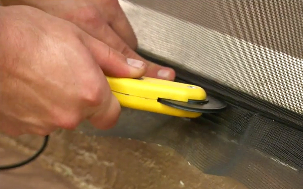 A person using a screen spline rolling tool to secure screen mesh into a base strip.
