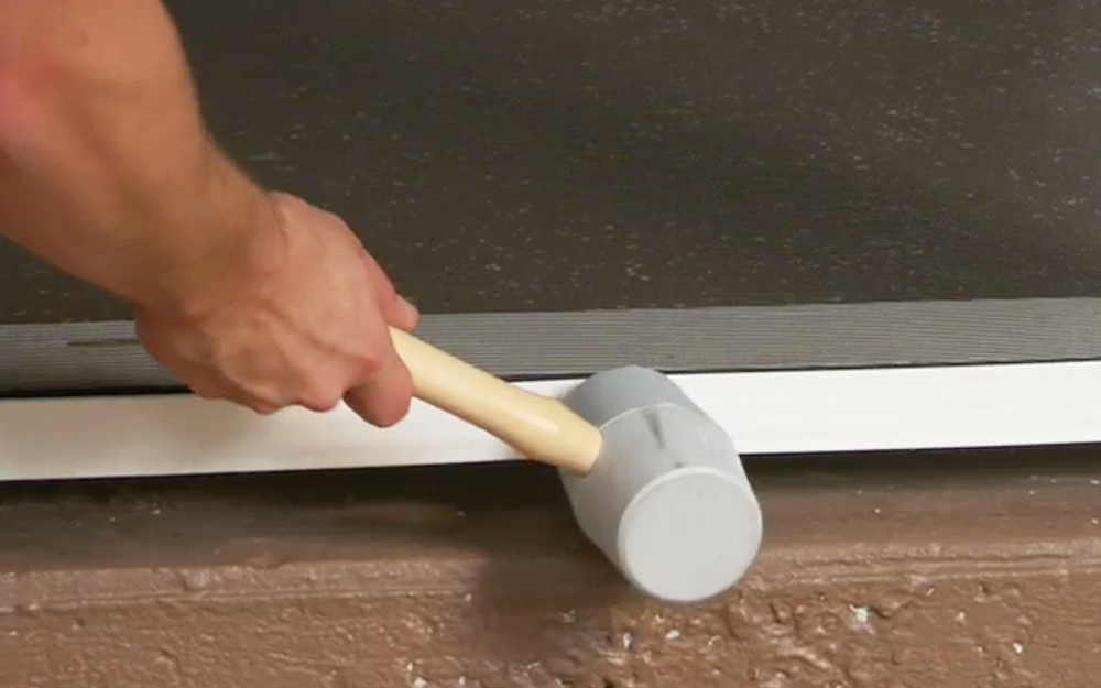 A person using a rubber mallet to secure a cap strip to a screen base..