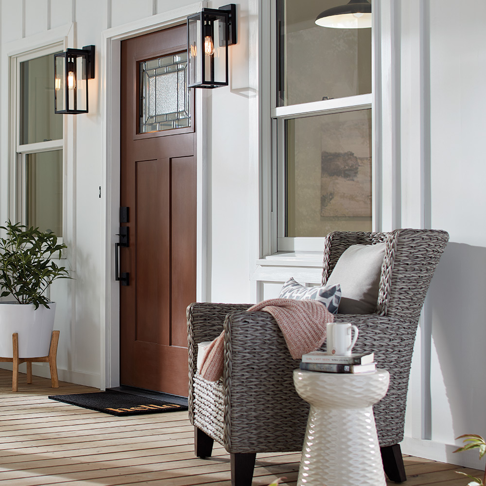 An outdoor chair sits next to a window and door with sconce lighting on a front porch.
