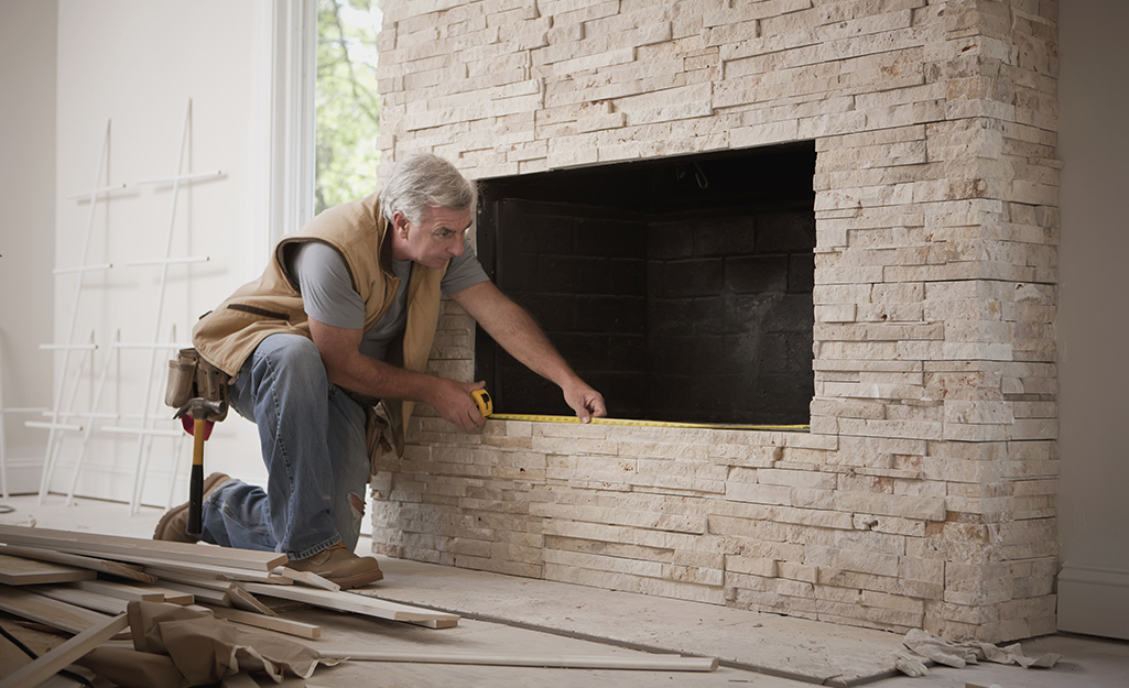 A man uses a measuring tape to measure a fireplace opening. 
