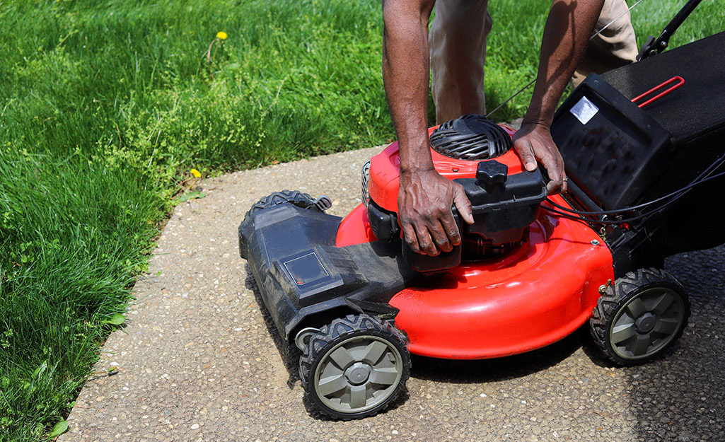 A person preparing a lawnmower for blade removal.