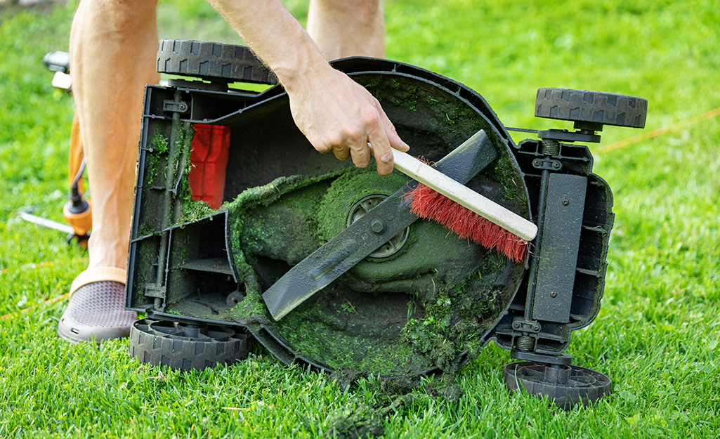 A person cleans the bowl around the lawn mower blade.