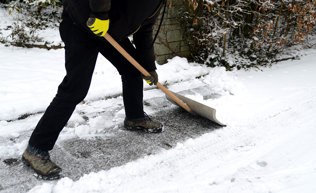 A person using a snow shovel to remove snow from a driveway.