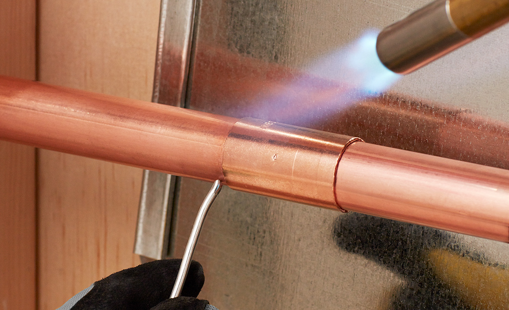 Someone soldering a copper pipe fitting.