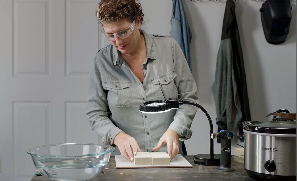 A woman places two bricks in the workspace where she will solder jewelry.