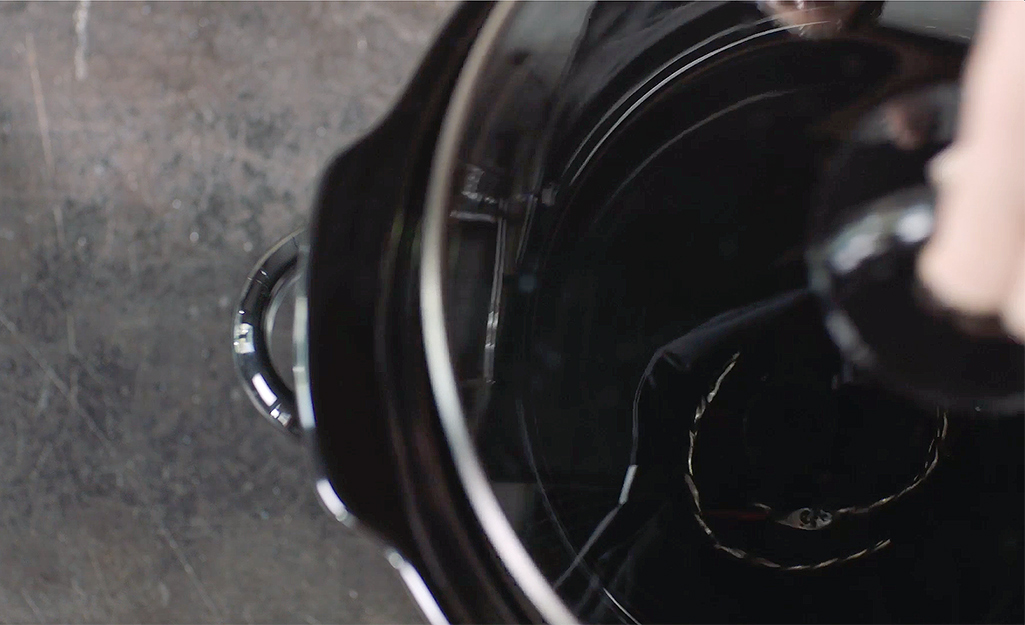 A person drops a necklace in a slow cooker to prepare it for soldering.