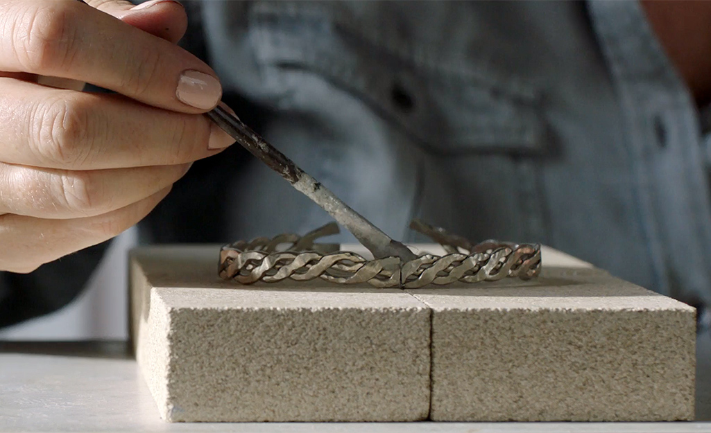 A person paints flux onto a bracelet with a paintbrush.