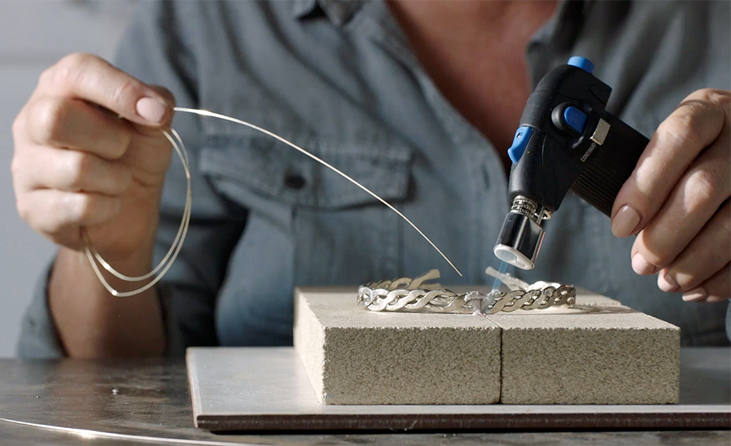 A person heats up a bracelet with a soldering iron.