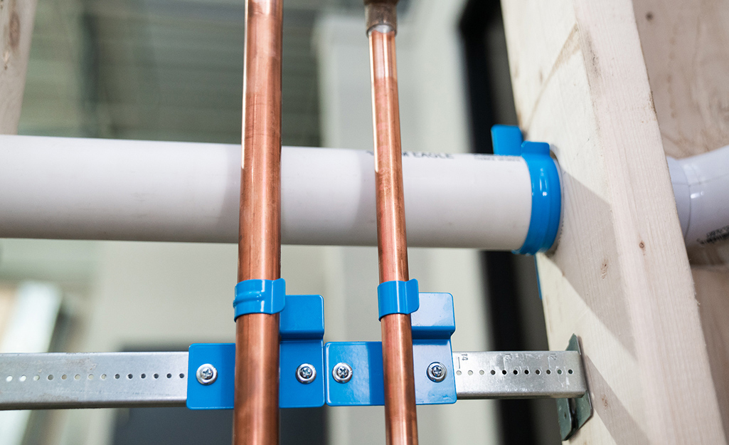 Two vertical copper pipes run in front of a horizontal PVC pipe.
