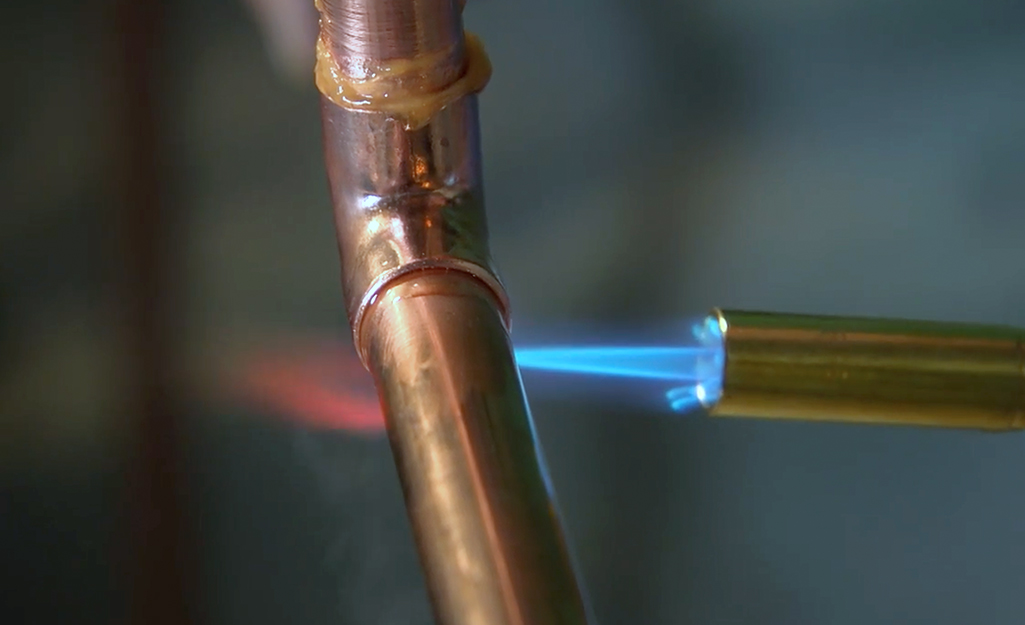 A soldering iron flame heats a copper fitting.
