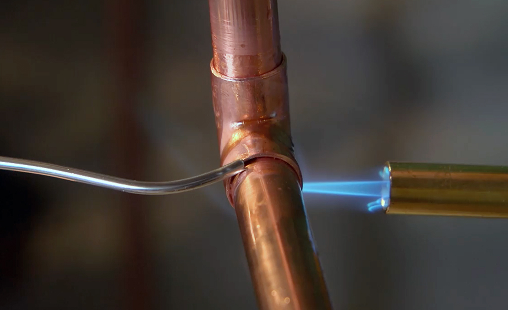 Someone applying solder to the joint between a copper fitting and pipe.