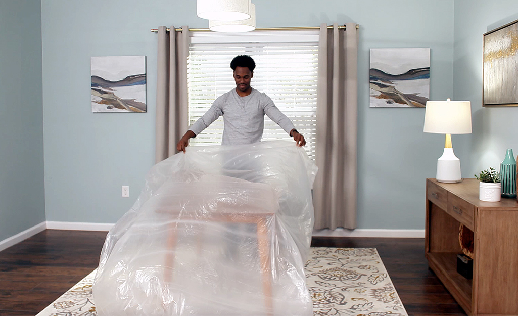 A person spreading out plastic sheeting before painting begins. 