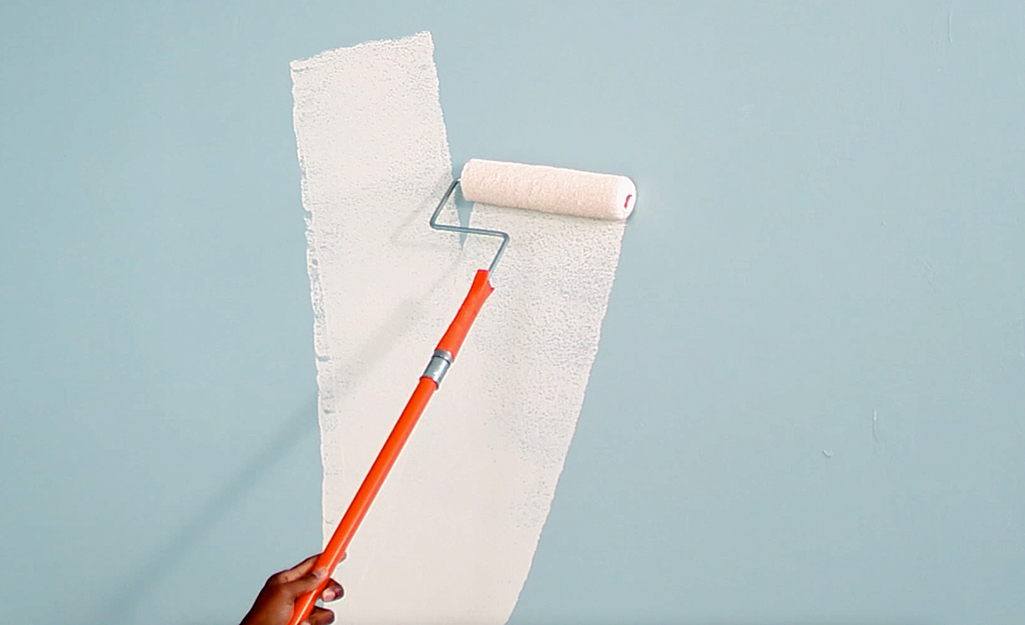 A person applies a base coat of paint to a wall.