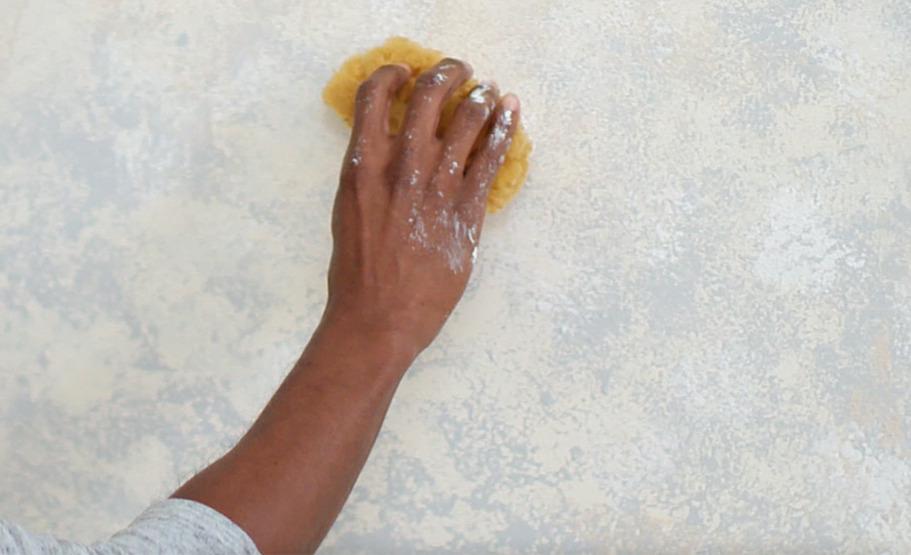 A person sponging a second color onto a wall.