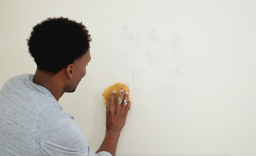A person sponging random paint patterns onto a wall.