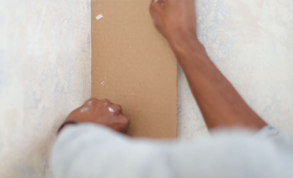 A person uses a piece of cardboard to apply paint to a wall corner.