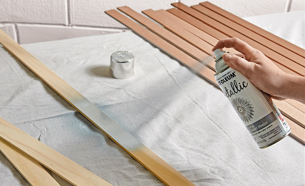 A person spray painting wooden slats with a can of silver paint.