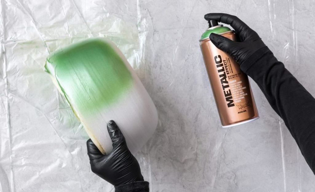 A person applying metallic spray paint to a clay bowl.