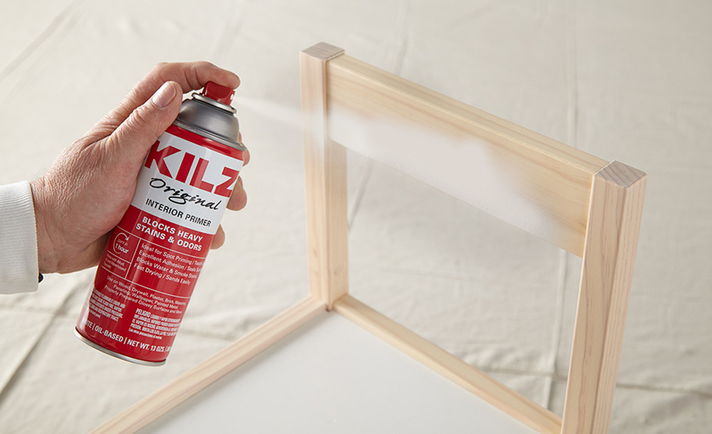 A person spraying a coat of primer paint onto a wood chair.