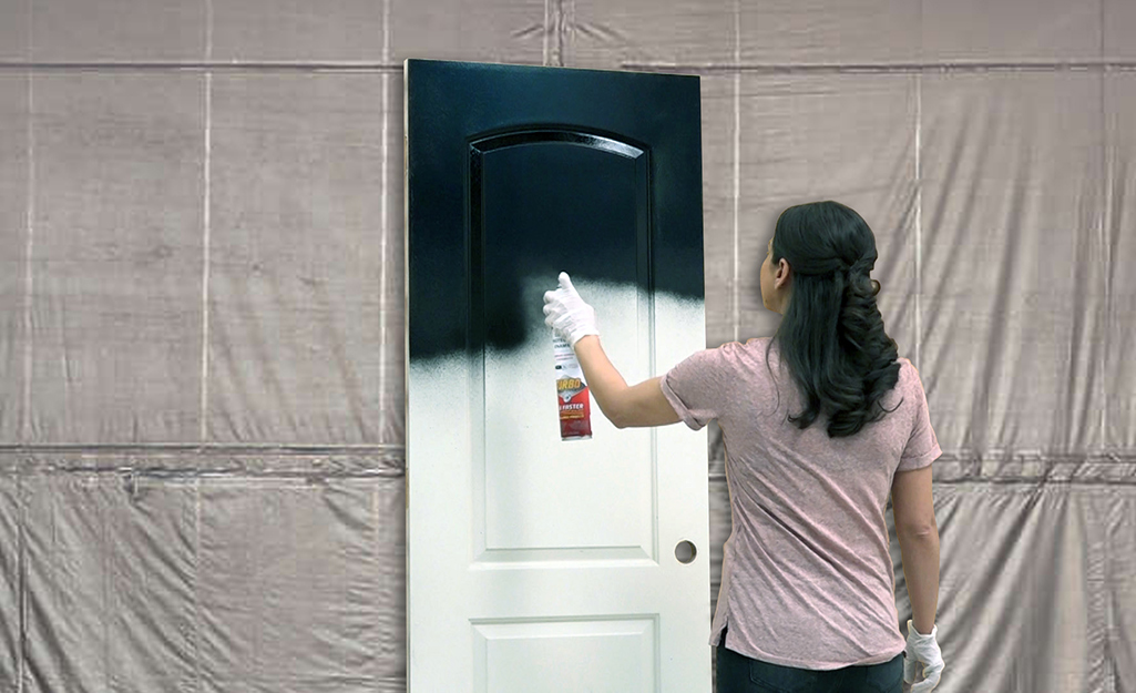 A person applying a coat of black spray paint to a primed door.