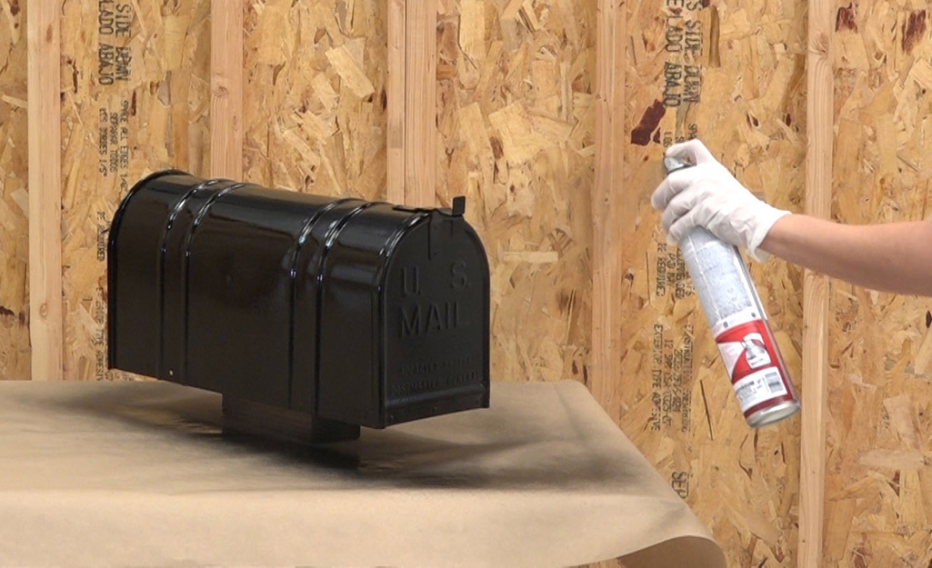 A person applying a coat of spray paint to a metal mailbox.