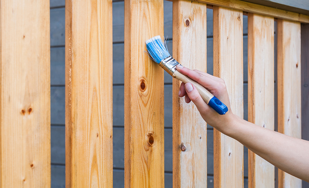 A person uses a paint brush to apply stain to the rails of a deck. 