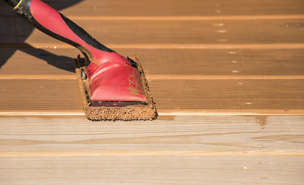 A person stains deck boards with a paint pad applicator. A person stains deck boards with a paint pad applicator.