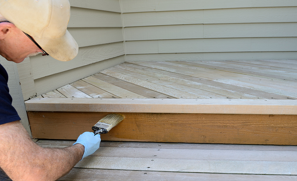 A person applies stain to a section of stairs on a deck.