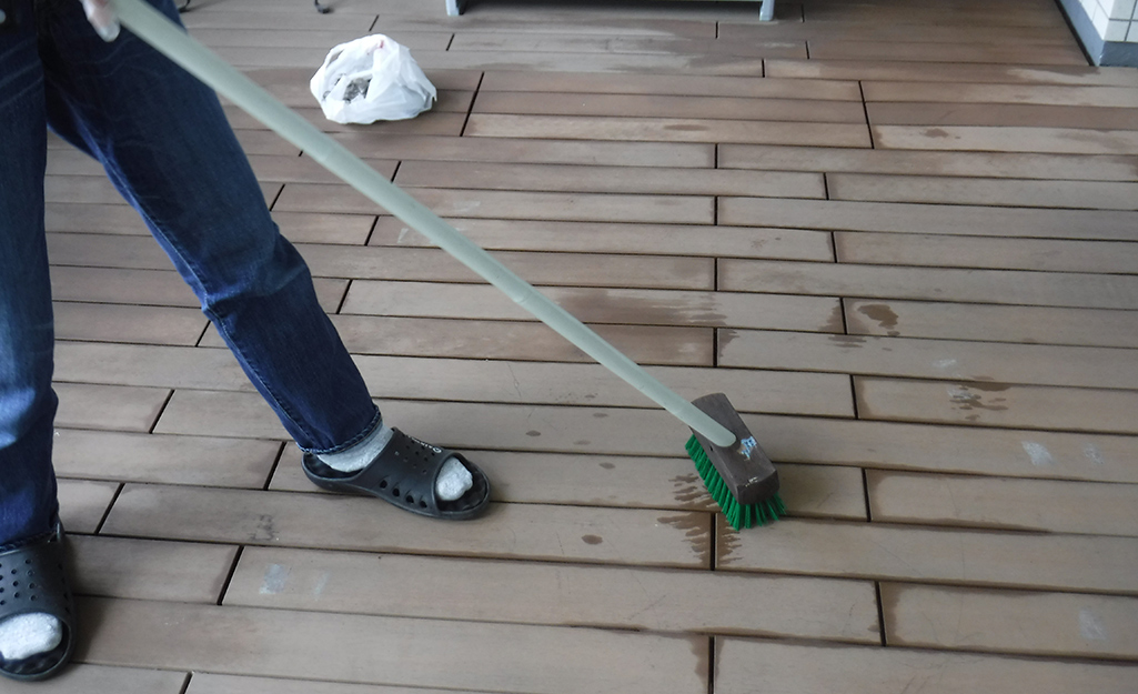 A person cleans a deck with a scrub brush. 