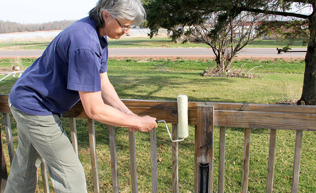 A person uses a roller to apply stain to the rails of a deck. 