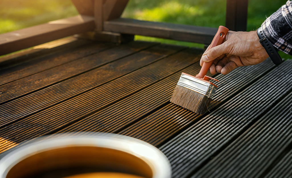 A person stains deck boards with a paint brush