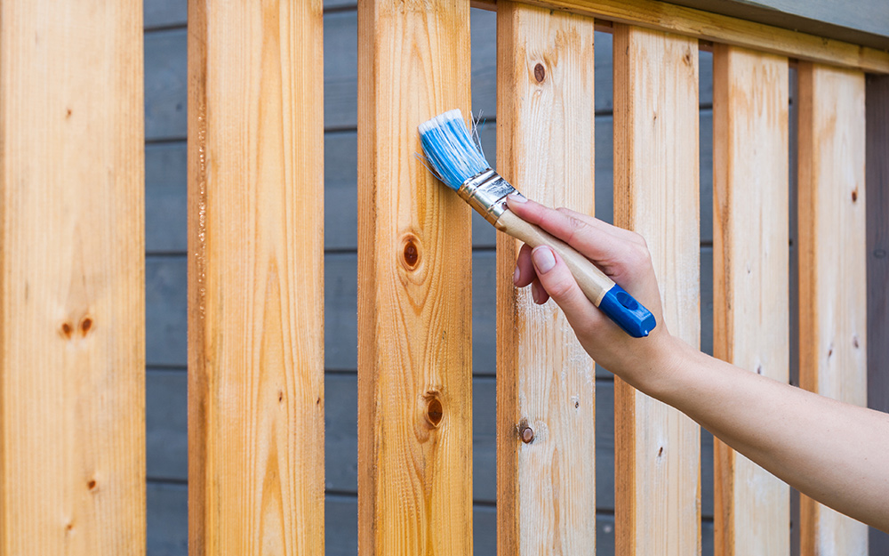 A person stains the balusters of a deck with a brush. A person stains the balusters of a deck with a brush.