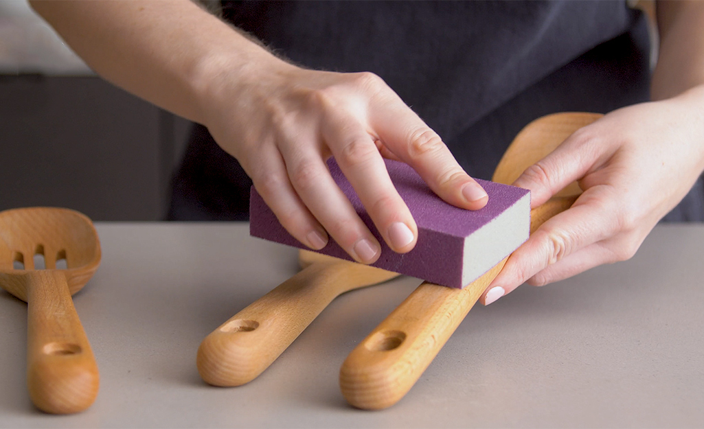 Wooden utensils are sanded using a sanding sponge. Wooden utensils are sanded using a sanding sponge.