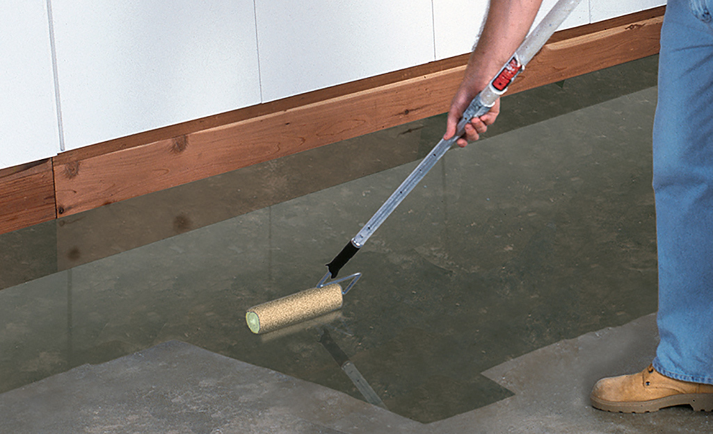 A person using a roller to apply sealer to a concrete floor.