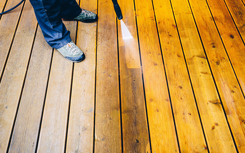 A person washes a pressure-treated wood deck with a sprayer.