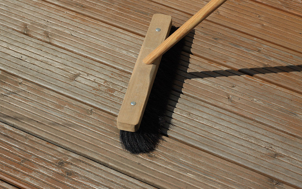A person sweeps a pressure-treated wood deck with a push broom.