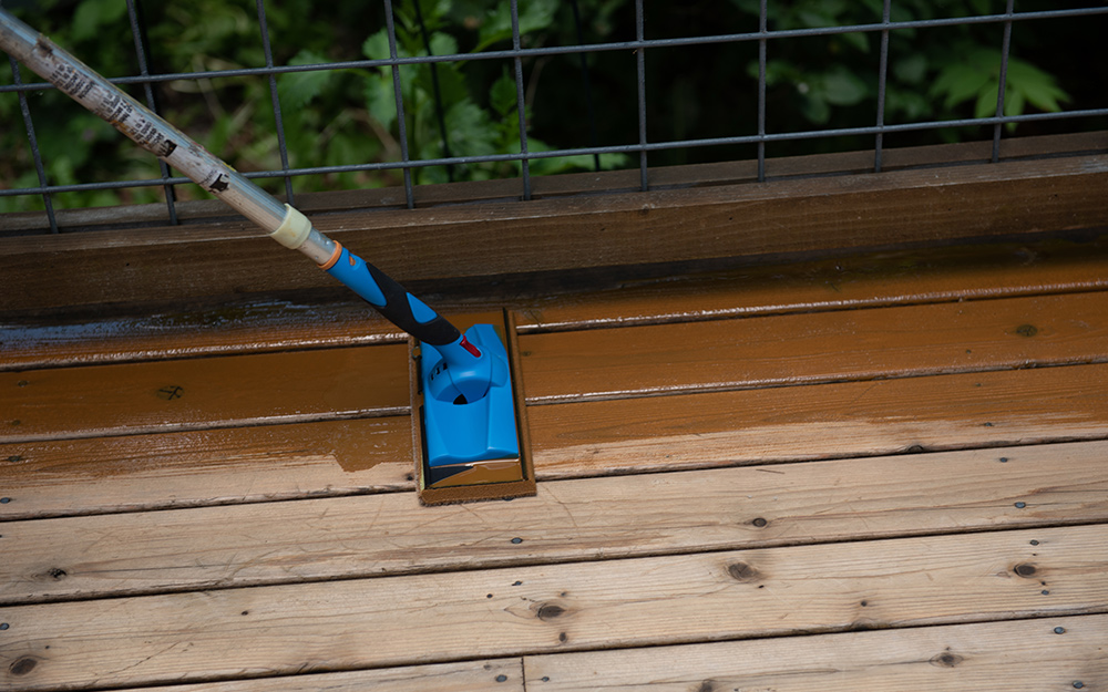 A person uses an applicator pad to apply stain to a pressure-treated wood deck.