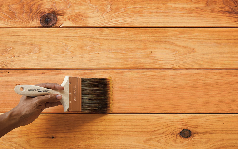 A person applies sealant to a pressure-treated wood surface with a brush.
