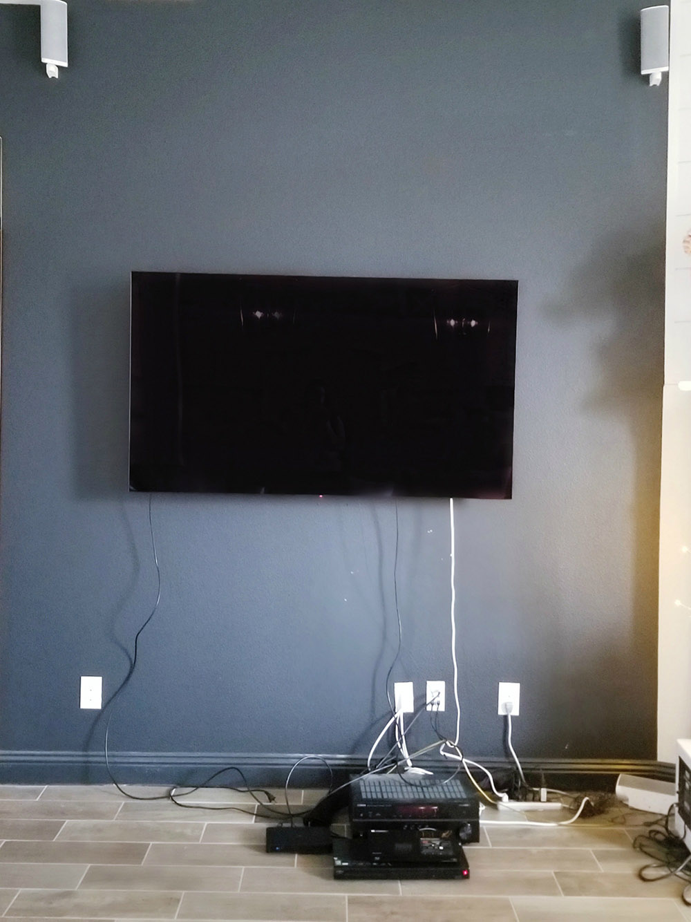 A flatscreen TV mounted on a dark wall with cords hanging down the wall.
