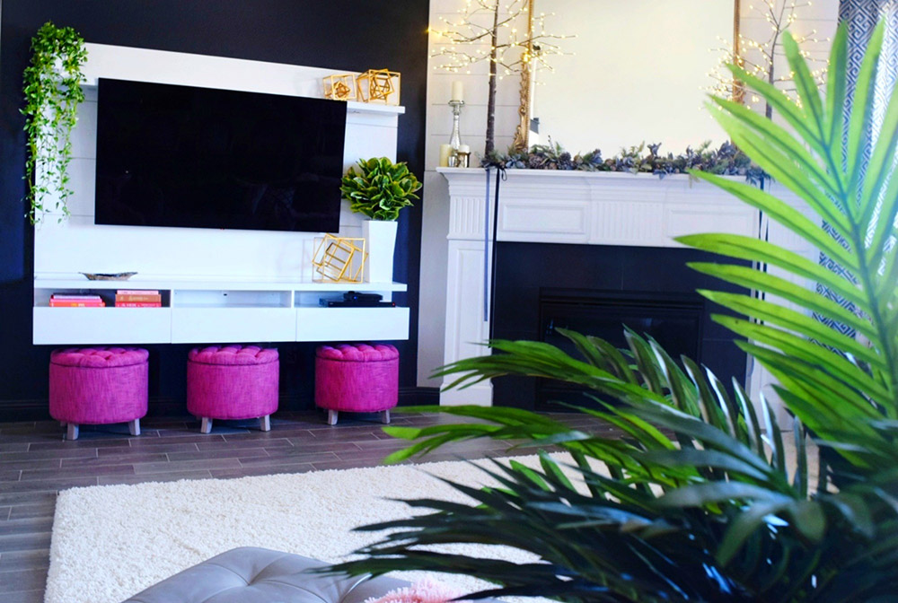 A trio of rose colored storage ottomans sit below a white floating entertainment center.