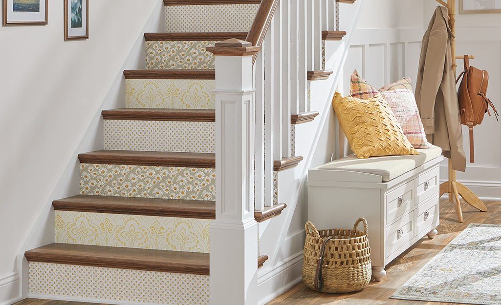An entryway staircase with wallpapered stair risers, storage bench and hat rack